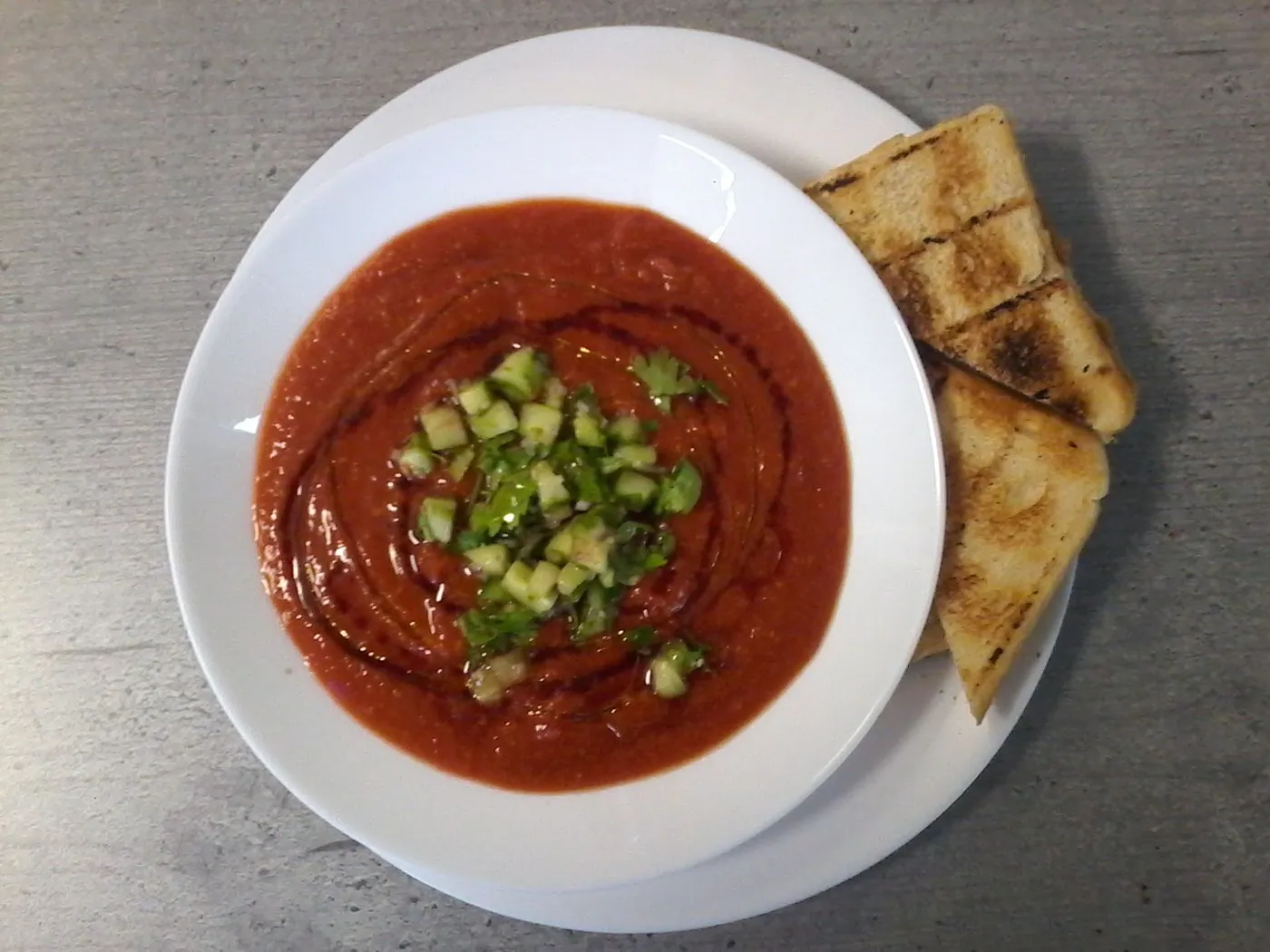 Tomatensuppe mit gewürfelter Gurke und geröstetem Brot.