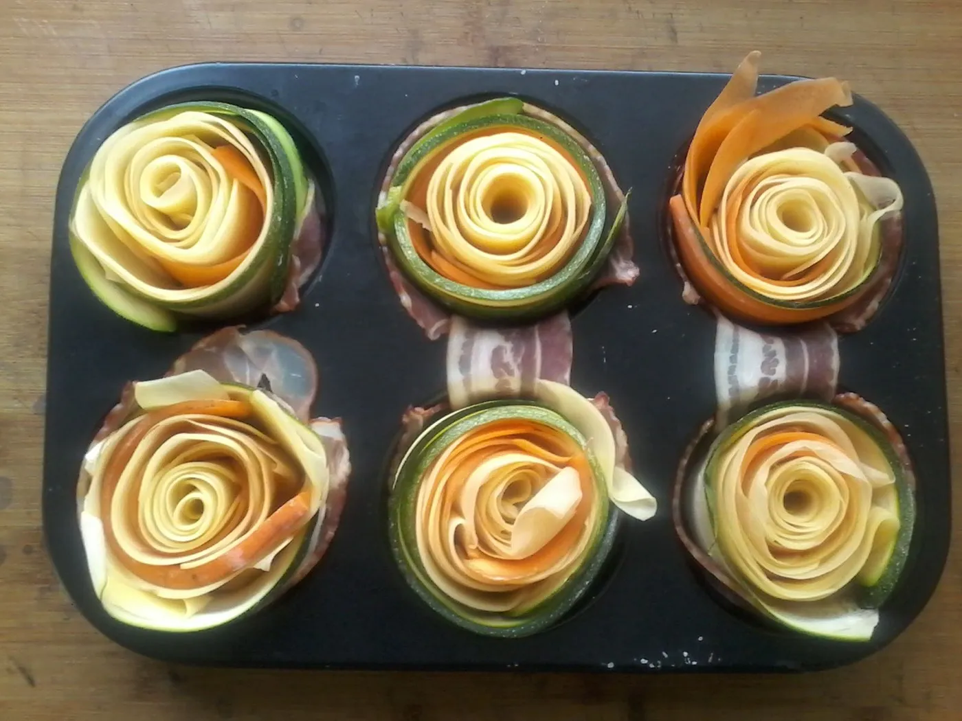 Zu Rosen gedrehtes Gemüse mit Speck in der Muffinform, vor dem Backen.